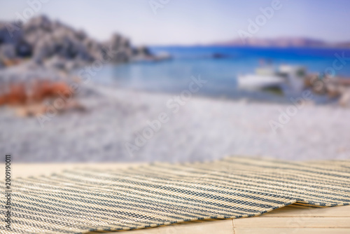 Minimal summer composition featuring clean sandy beach with empty copy space for product placement. Rocky coastline meets the sea under bright blue sky, creating natural and scenic atmosphere.