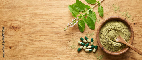 herbal medicine concept with kratom powder and capsules on wooden table with fresh leaves