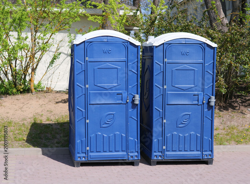 Two Blue Portable Toilets Side-by-Side in Public Park — Photo of Mobile WC Units, Outdoor Event Sanitation, and Public Restroom Infrastructure