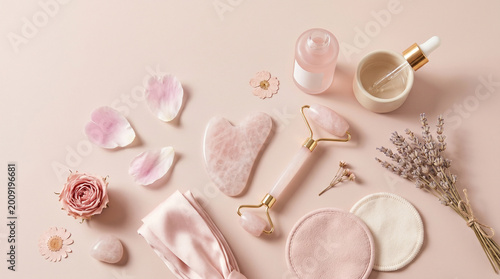flat lay of pink skincare tools and flowers on pastel background for beauty wellness concept