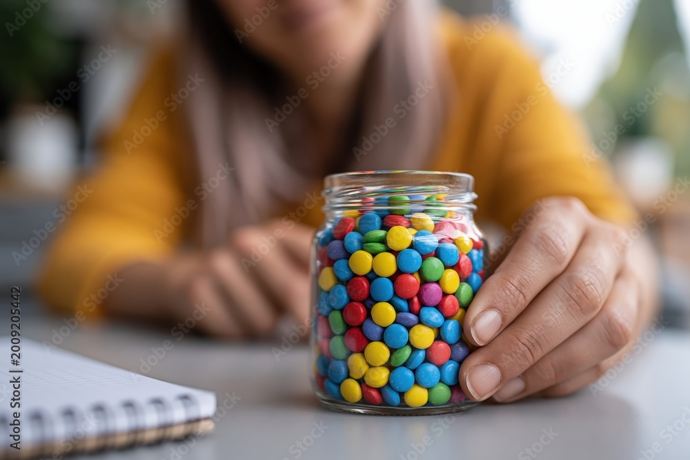 Fototapeta premium Adult hand placing colorful tokens in glass jar for progress tracking at home office desk