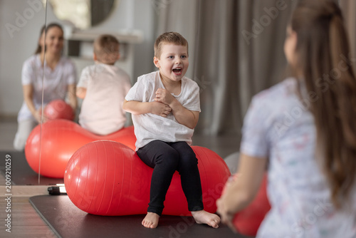 Child Physical Therapy Session With Therapist Using Red Exercise Ball In Pediatric Rehab Clinic