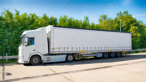 White semi truck with trailer parked on roadside, freight transport and logistics concept, commercial delivery vehicle for cargo shipping and trucking business. Copy-space.
