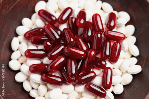 A pile of Omega-3 nutritional capsules and white collagen protein pills in a brown wooden container. Supplements mix.