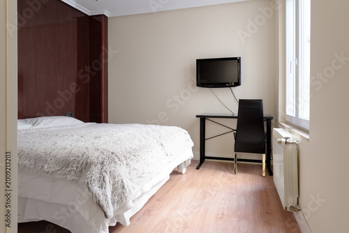 Compact economy hotel room with a minimalist workspace. Double bed and wall mounted TV. Practical budget-friendly interior