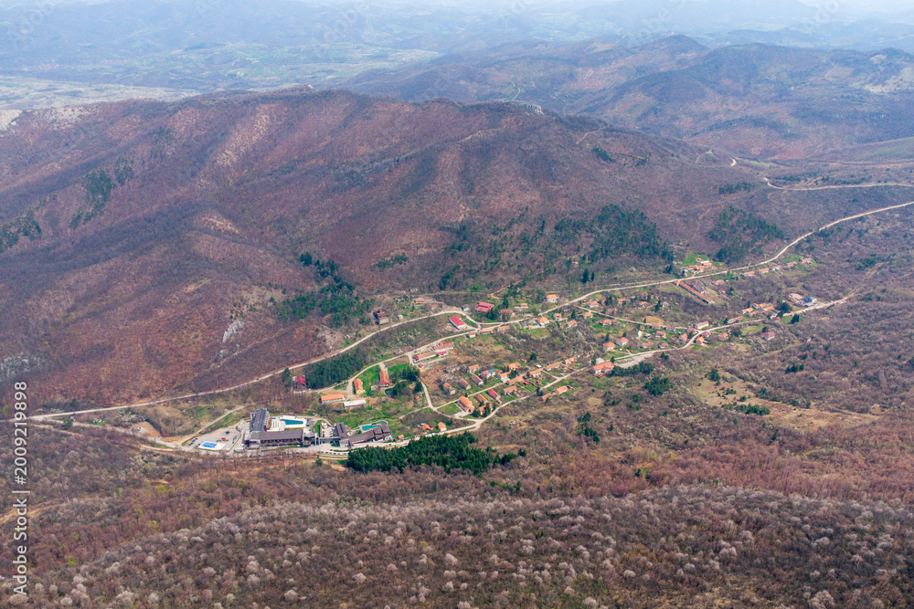 Fototapeta premium High angle view of a remote mountain village and resort nestled among the hills and forests, with roads winding through the valley