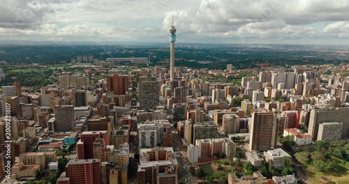Aerial wide panning shot across Johannesburg skyline featuring Hillbrow Tower. Dramatic drone panorama of South African urban landscape, dense city architecture, and metropolitan horizon.
