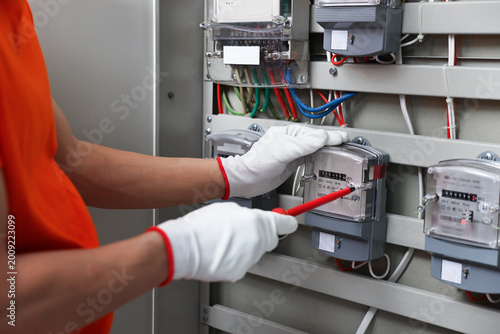 Fotografie Electrician with screwdriver checking electrical meter indoors, closeup
