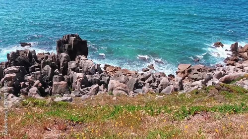 Atlantic waves crash against a jagged rocky shore and sea caves, capturing the powerful rhythmic motion of the ocean against a wild, rugged coastline under bright daylight.