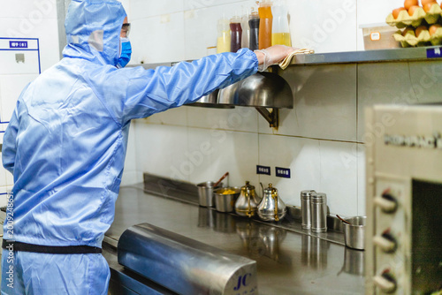 Protective worker disinfecting restaurant kitchen counter for safe reopening