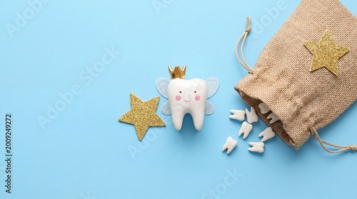 Tooth fairy character with a crown and wings next to a bag of teeth on a blue background. Childhood, tradition, tooth loss, magical concept.
