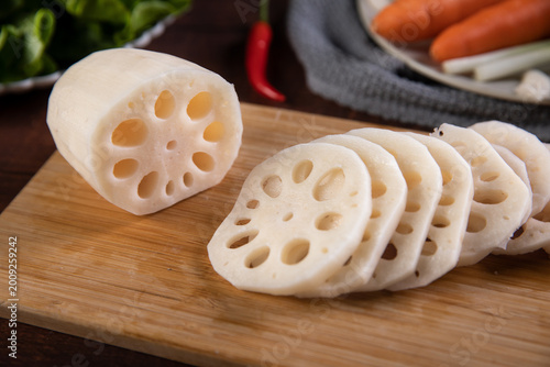 Slika na platnu Fresh sliced lotus root on wooden cutting board with vegetables