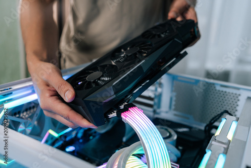 Person upgrading gaming computer, installing powerful graphics card into open pc case, showing internal components with rgb led lighting and custom liquid cooling system, close-up.