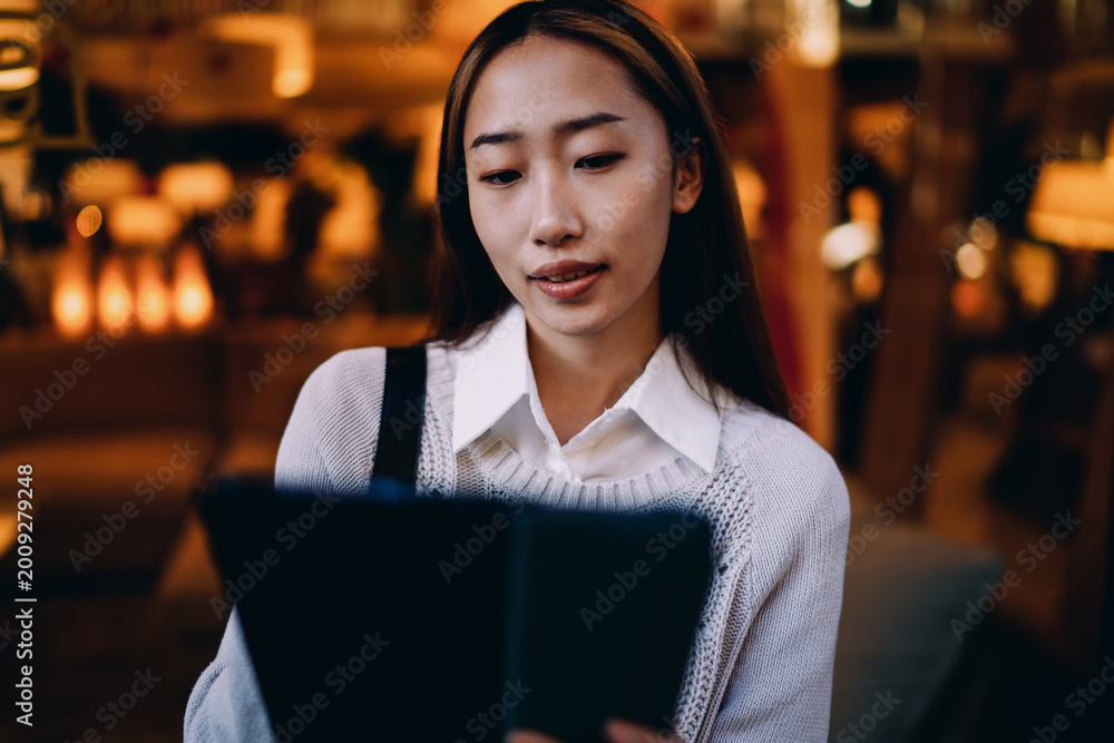 Fototapeta premium Asian woman focused on tablet screen outdoors. Captures immersive attention, remote productivity, and confidence with mobile tech in realistic freelance setting.