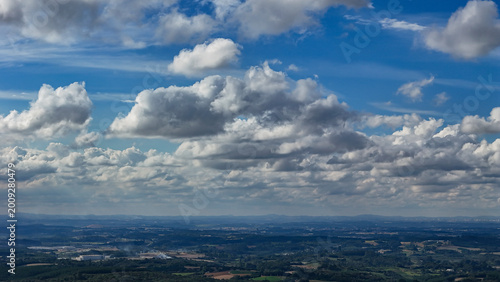A wide-angle composition that highlights the contrast between a dynamic, cloud-laden sky and the vast, varied vegetation at its base.