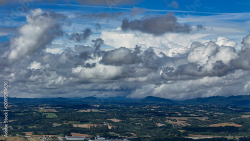 A wide-angle composition that highlights the contrast between a dynamic, cloud-laden sky and the vast, varied vegetation at its base.