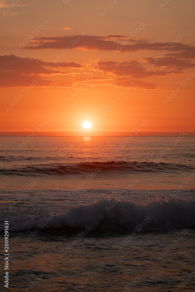 Fototapeta premium Golden sunset over ocean waves with dramatic orange sky