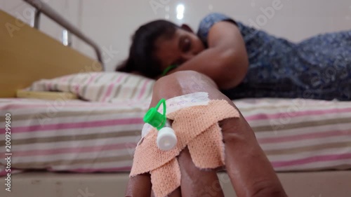 Person resting on a bed while receiving medical treatment in a simple hospital room during the day