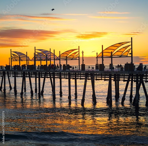 Принти на полотні Sunset at Redondo Beach Pier with silhouettes of people and warm ocean reflections under a colorful evening sky