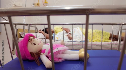 Child rests in hospital bed while stuffed doll waits nearby in the bright room during a medical check-up