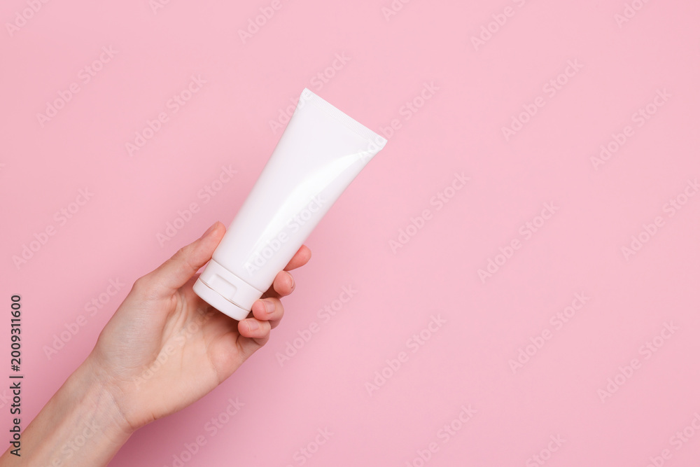 Fototapeta premium Woman holding tube of hand cream on pink background, closeup. Space for text