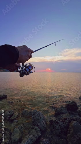 Vertical video. Hand Holding Fishing Rod Toward Sea Sunset First Person View Close Angle Outdoor Angling Action Horizon Reflection