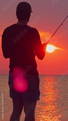 Vertical video. Man Silhouette Fishing Against Bright Sunset Over Sea Horizon Warm Light Reflection Coastal Outdoor Angling Lifestyle