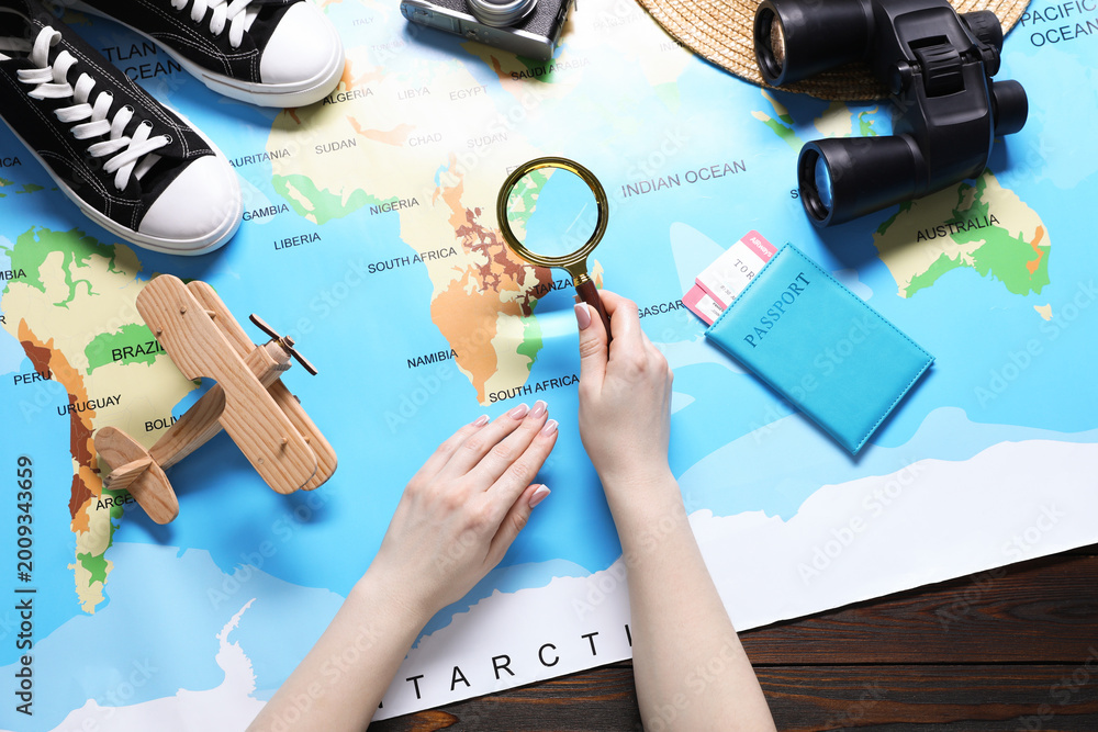 Fototapeta premium Woman with magnifying glass and world map planning trip at wooden table, top view
