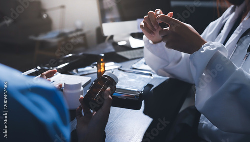 Female doctor holding a medicine bottle is checking the quality of medicine for any side effects the patient or not and recording patient information at the hospital. medical and health care concept