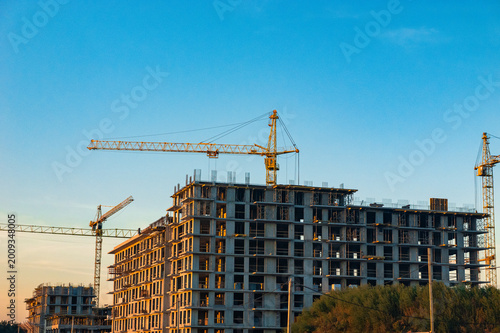 A modern apartment building under construction is shown with cranes against a vibrant sunset sky. It symbolizes growth, development, and the ongoing evolution of urban landscapes.