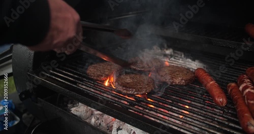 Summer barbecue BBQ cook flips flame grilled burger and hot dog sausages