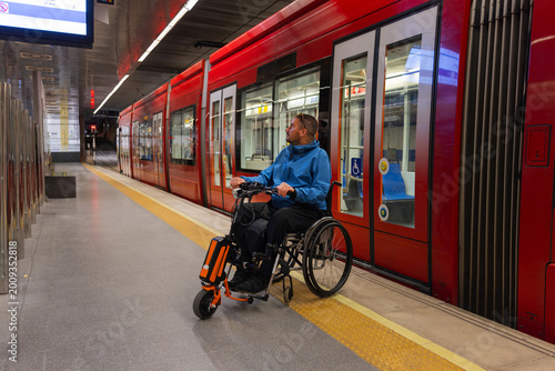 Person with disability on wheelchair waits at the metro station for accessible transport to arrive.