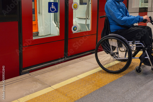 Person with disability on wheelchair waits at metro station for accessible transport.