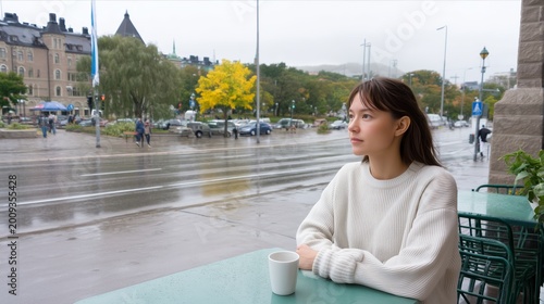 Beautiful young woman sitting at an outdoor sidewalk cafe on a rainy day. Calm, relaxing, and melancholy lifestyle concept.