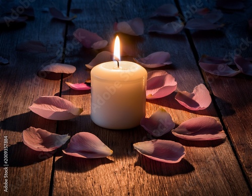 solitary flickering candle flame surrounded by delicate petals on rustic wooden surface at dusk symbolizing solemn memorial and mournful tribute for remembrance of wrongful death