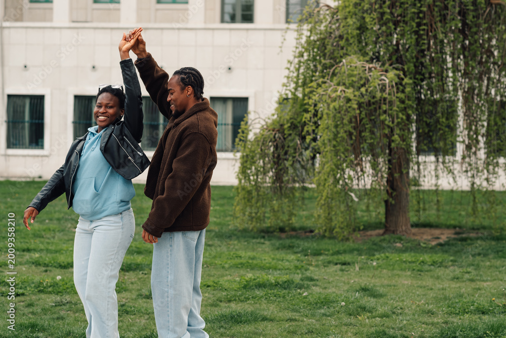 Fototapeta premium Happy african american couple dancing together in a park. Man and woman enjoying a relaxed day out, sharing happiness