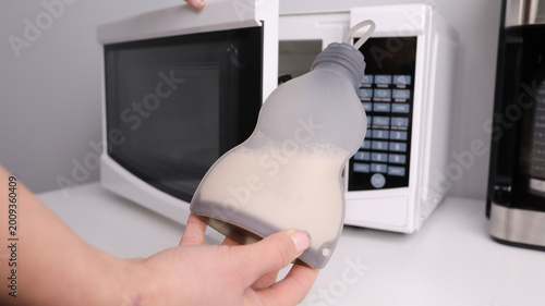 Fotografie Person holding a silicone breast milk storage bag in front of a microwave, concept of improper milk warming and baby safety