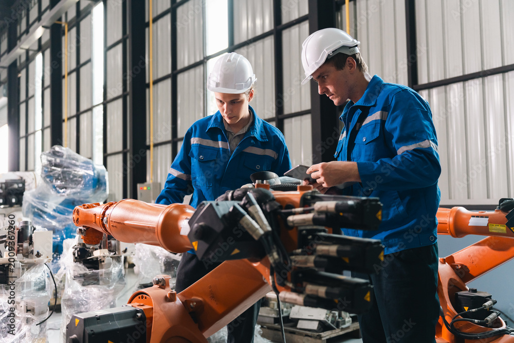 Obraz premium Robot arm worker engineer auto manufacturing factory teamwork inspection industrial technology safety helmet uniform mechanic technician man machine automation modern equipment assembly line