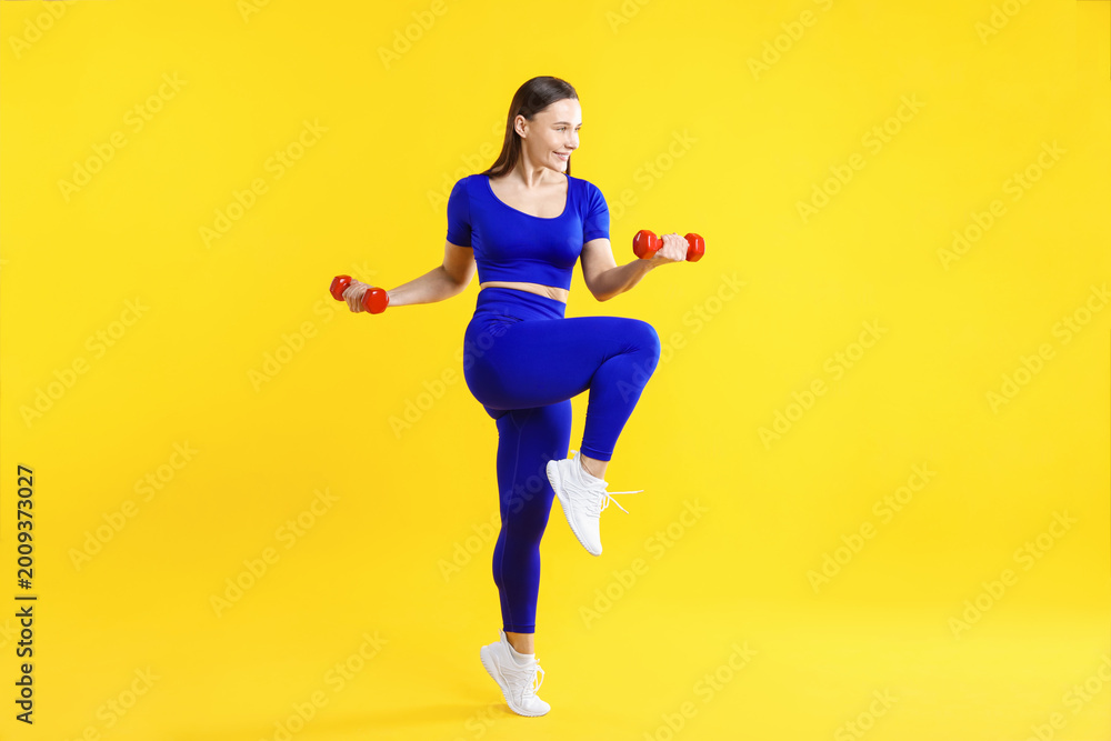 Fototapeta premium Woman in sportswear with dumbbells on yellow background