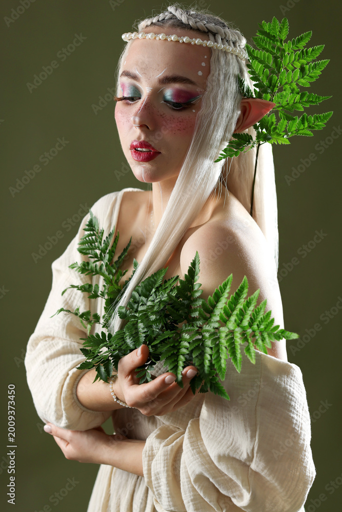 Fototapeta premium Beautiful elf girl with floral decor on dark olive background
