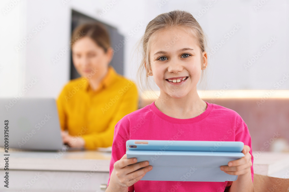 Obraz premium Cute girl with tablet and her mother using laptop at home, selective focus