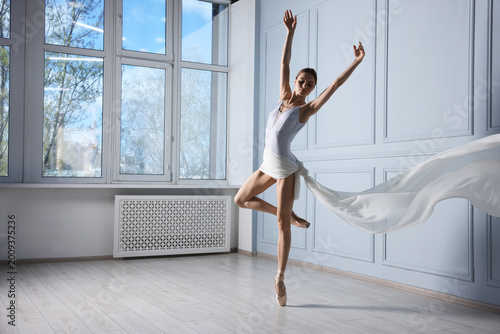 Bilde på lerret Graceful ballerina with white veil practicing dance moves near grey wall in studio