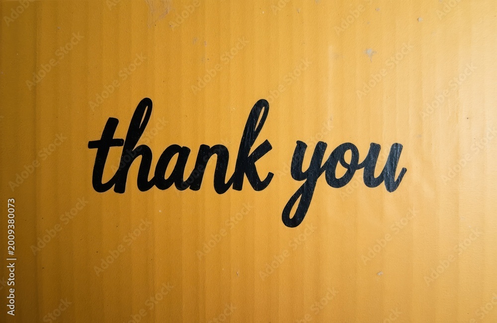 Naklejka premium Black script text saying thank you printed on rough yellow cardboard. Simple appreciation message on textured box surface, copy space available for design.