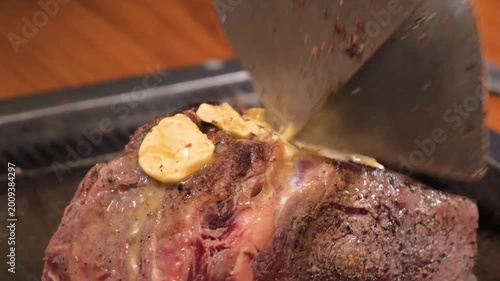 Slow-motion close-up of a professional chef carving a perfectly cooked, medium-rare prime rib roast beef at a restaurant carvery station. The meat is seasoned with cracked black pepper and topped with