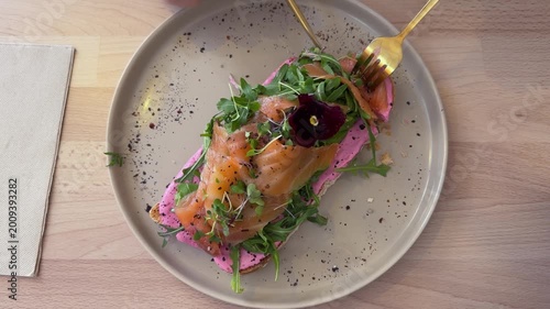 Male hands holding cutlery cutting through Smoked salmon toast with microgreens and edible flower