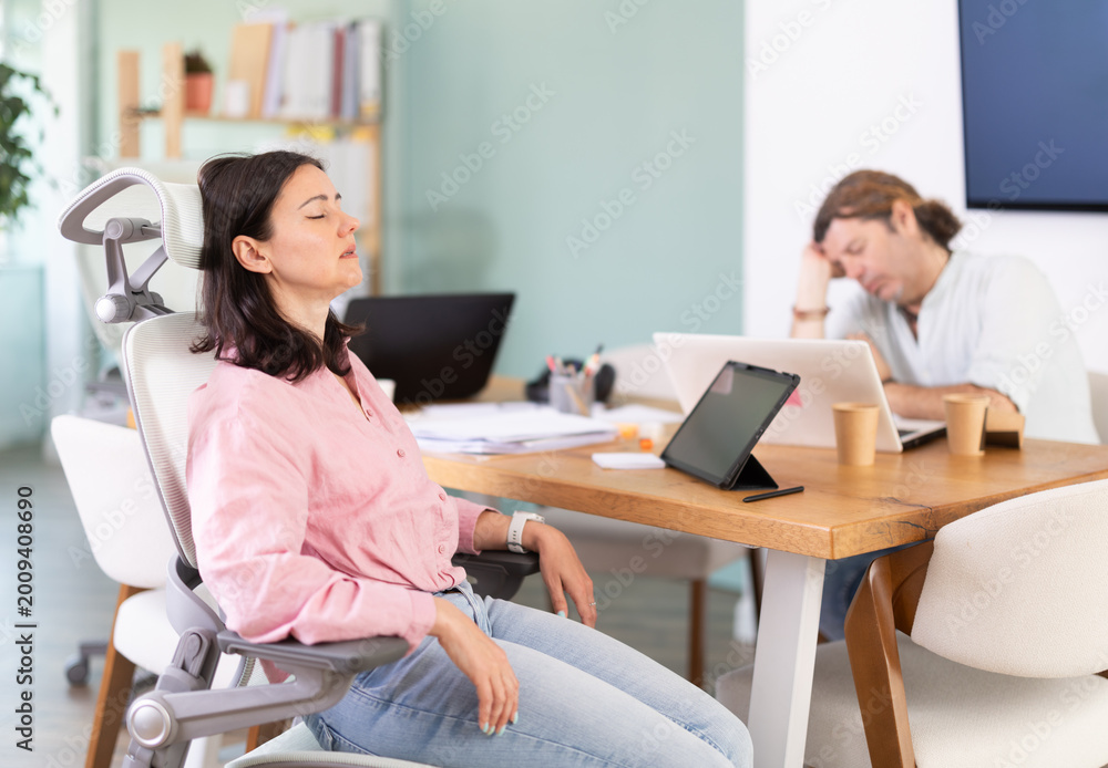 Obraz premium Tired adult woman and male colleague fall asleep while working on laptop in office