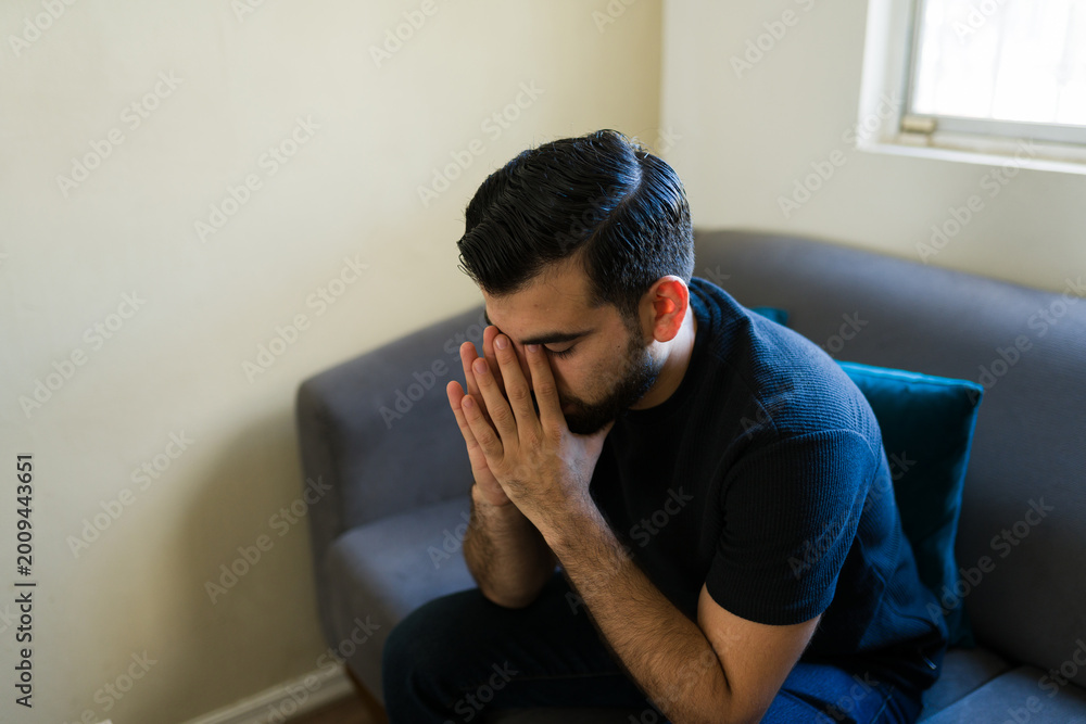 Obraz premium Young man covering face with hands showing sadness, depression, anxiety, despair, and mental health issues