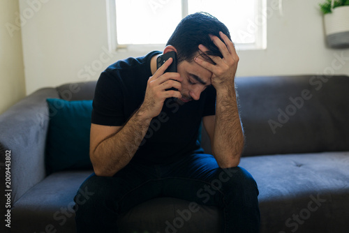 Tableau sur toile Stressed man sitting alone on sofa making a phone call, feeling lonely and seeki