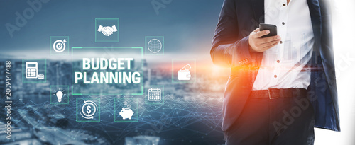 Quadro em tela Professional Man Engaging in Budget Planning with Smart Phone in Modern Cityscape Background Featuring Various Financial Icons and Graphics Fluxor