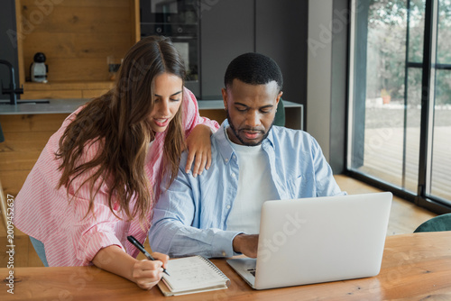 Foto A couple collaborates at their kitchen table, using a laptop and notebook to plan finances, schedule tasks and projects while sharing ideas and staying focused in a bright modern home setting